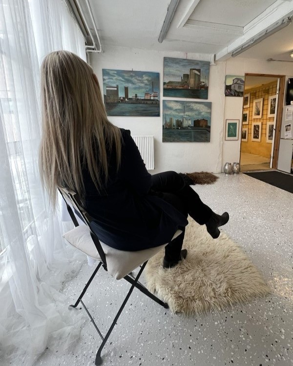 Grethe sidder i udstillingen og kigger på hendes kunst